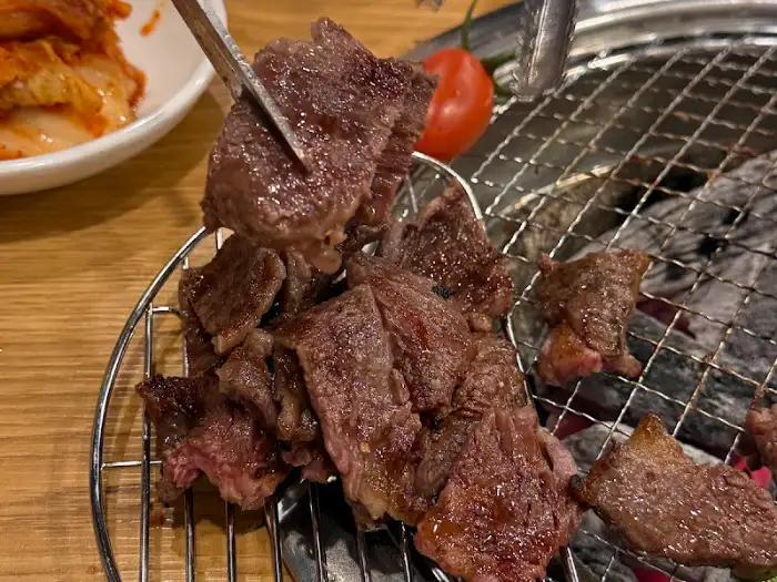 고기가 숯불 위에서 잘 익어가고 있으며, 옆에는 김치와 토마토가 보인다.
