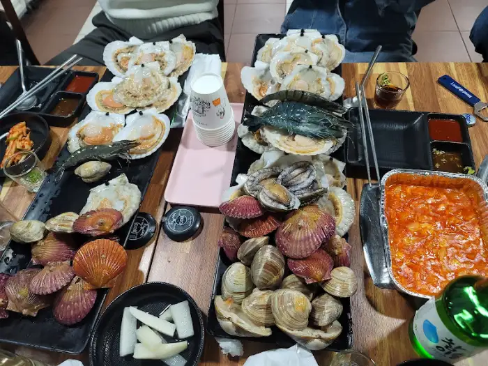 다양한 종류의 조개와 새우, 그리고 불판 위에 올려진 조개구이의 전체 모습.
