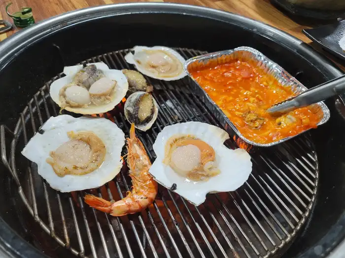 호일 용기에 담겨 숯불 위에서 조리되는 조개와 새우.