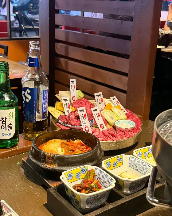 테이블에 놓인 술병, 밥, 찌개, 그리고 고기 플레이트