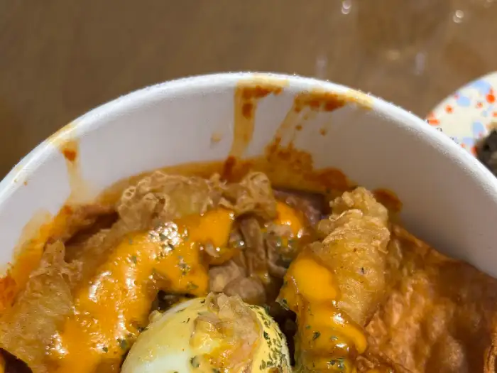 컵에 담긴 떡볶이 클로즈업, 치즈가 뿌려져 있고 튀김 조각들이 보인다.