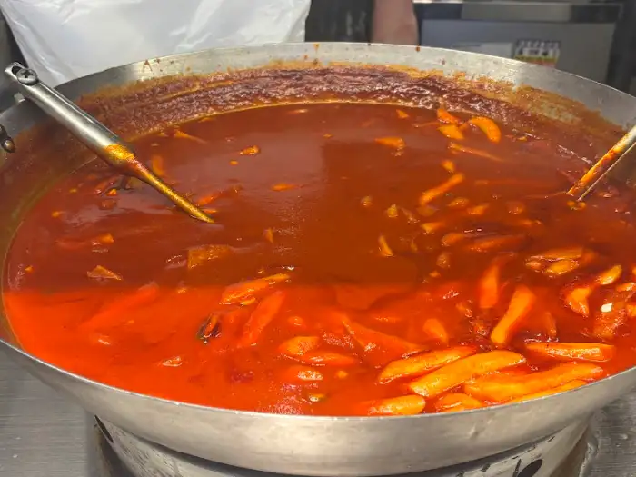 큼직한 솥에 떡볶이 국물이 붉게 끓고 있는 모습. 떡과 다양한 재료들이 보인다.