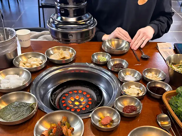 테이블 위에 차려진 다양한 반찬과 숯불 구이 불판