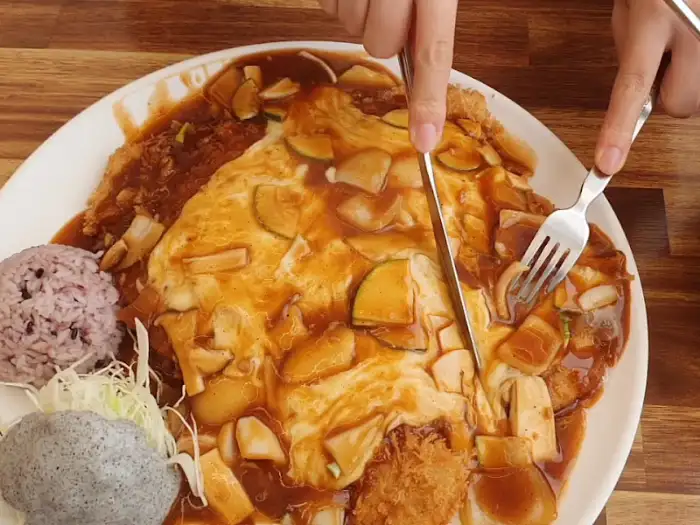 소스가 듬뿍 얹어진 돈까스를 썰고 있는 모습