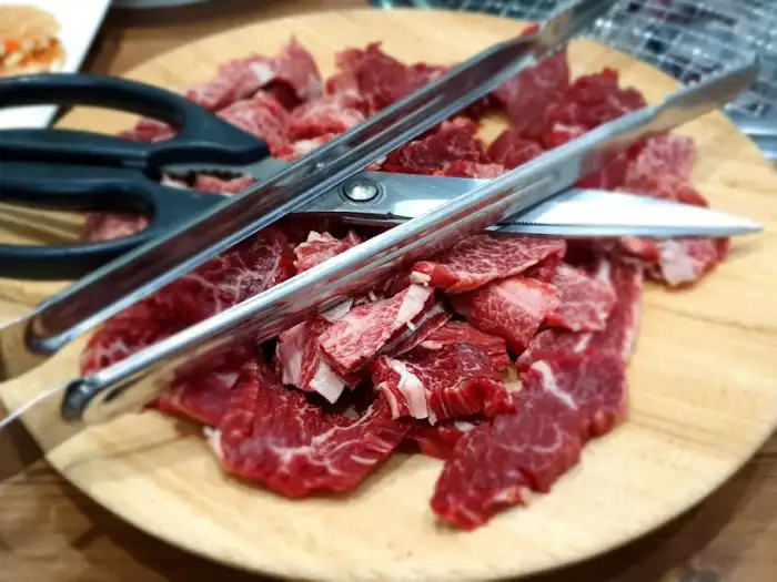 도마 위에 놓인 고기 덩어리와 집게, 가위