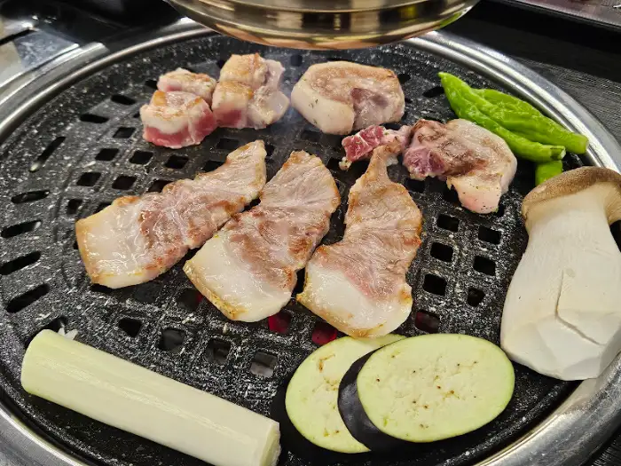불판 위에서 익어가는 다양한 고기 부위와 채소