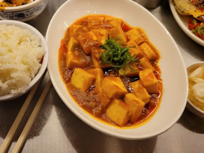 흰 쌀밥 옆에 놓인 마파두부. 큼직한 두부 조각들이 매콤한 소스에 잠겨 있고, 위에 파채가 고명으로 올라가 있다.