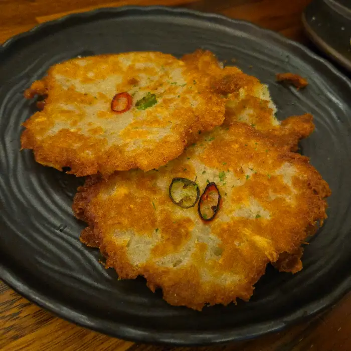 따뜻하게 구워진 두 장의 감자전이 검은 접시에 담겨 있는 모습