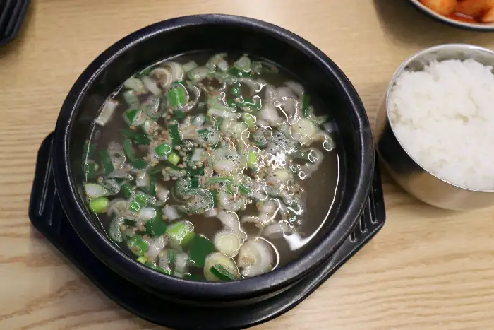 검은 뚝배기에 담긴 곰탕으로, 맑은 국물에 파와 고기가 들어있습니다.