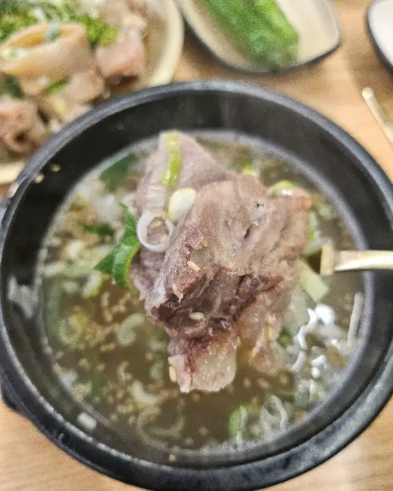 숟가락으로 곰탕 국물에 들어있는 고기를 건져 올리고 있는 모습