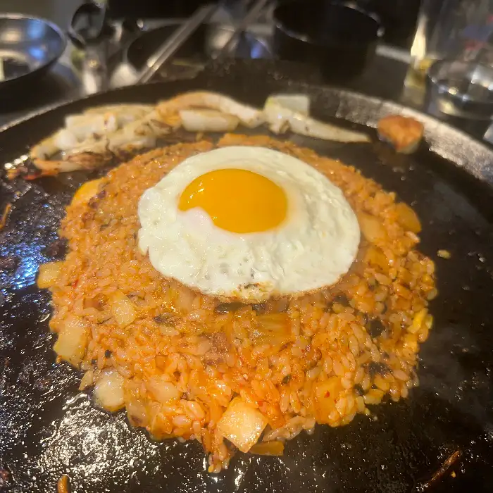솥뚜껑 위에 구워지고 있는 삼겹살과 콩나물, 김치 등의 모습