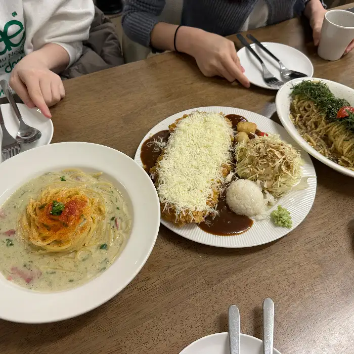크림소스 파스타, 눈꽃치즈 돈까스, 깻잎 파스타가 테이블에 놓여 있는 모습.