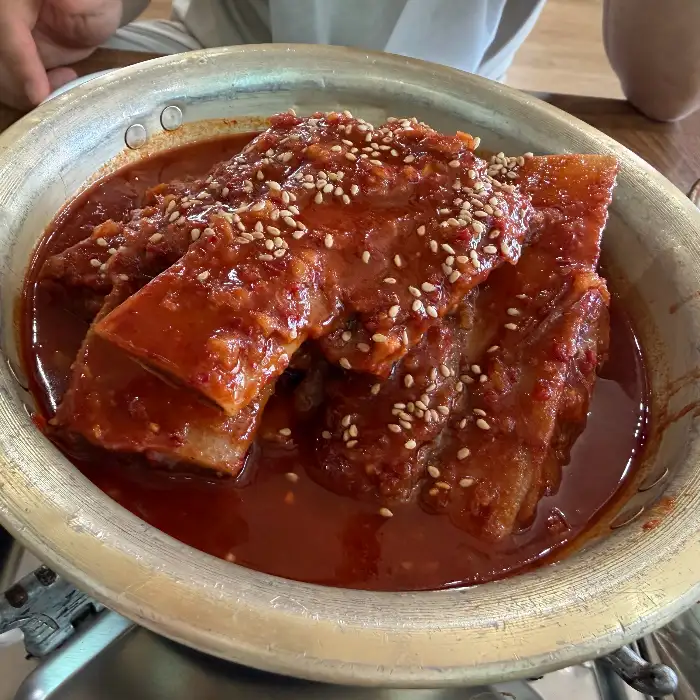 갈비찜 냄비의 클로즈업, 붉은 양념에 버무려진 푸짐한 갈비와 깨소금