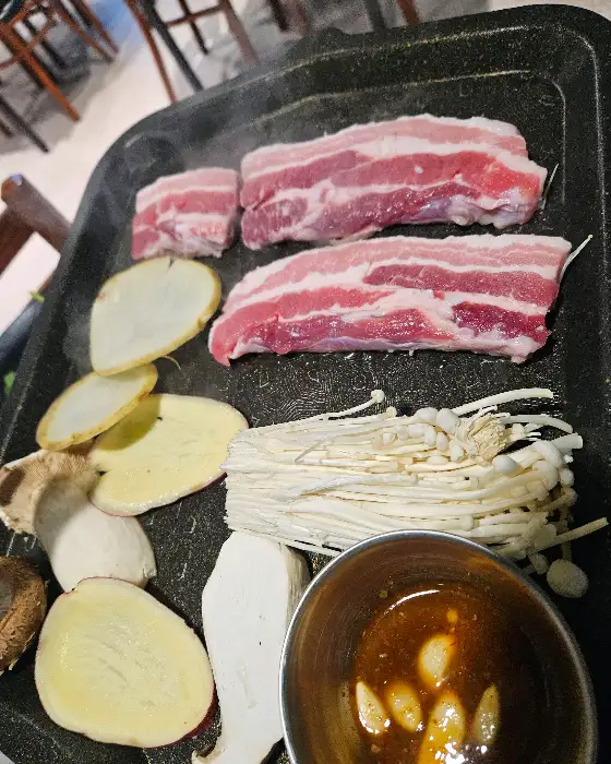 불판 위에 올려진 삼겹살, 감자, 버섯 등