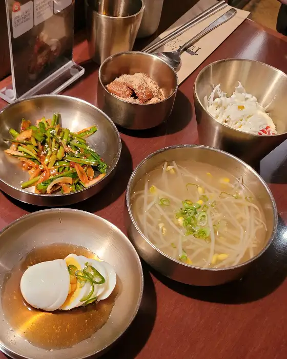 테이블 위 쟁반에 담긴 채소 무침, 삶은 계란, 그리고 콩나물국