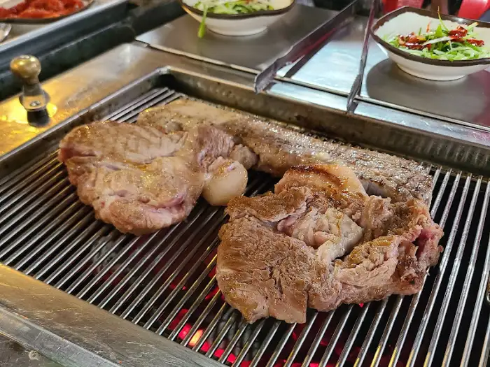 숯불 위에서 구워지는 두툼한 삼겹살과 함께 더덕구이가 올라와 있습니다.