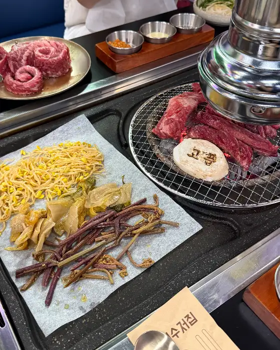불판 위에 고사리, 묵은지, 콩나물 등과 함께 구워지고 있는 대패 삼겹살