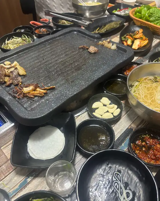 잘 달궈진 불판 위에 올려진 신선한 소고기와 다양한 반찬들