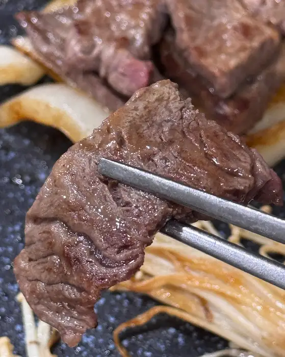 집게로 집어 올린 잘 익은 소고기 한 점