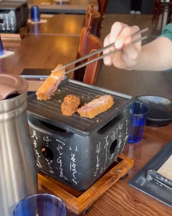 젓가락으로 규카츠 조각을 개인 화로에 올려 굽는 모습
