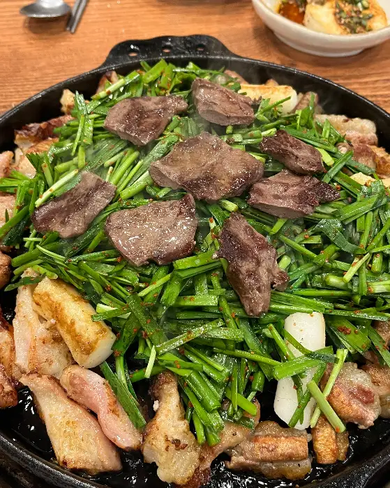 싱싱한 곱창과 대창, 그리고 그 위를 덮은 신선한 부추가 함께 구워지고 있는 모습.