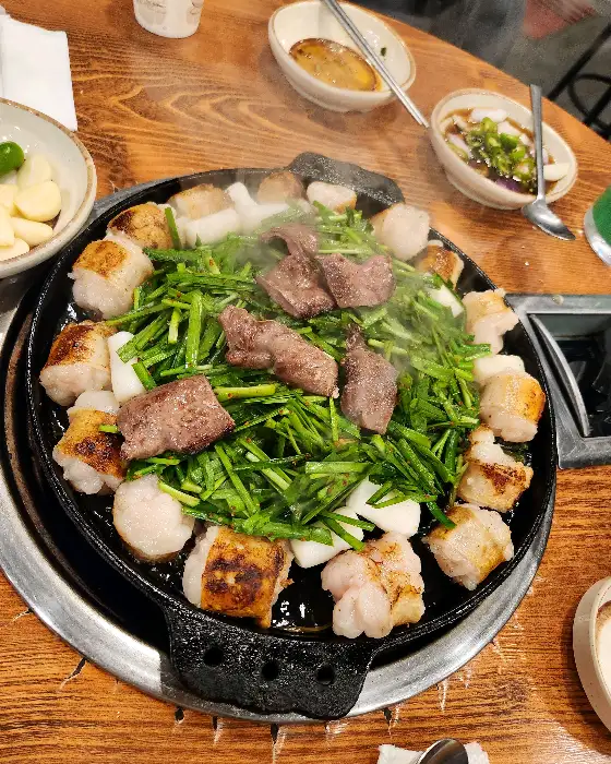 잘 구워진 곱창, 대창, 그리고 부추가 불판 위에 먹음직스럽게 담겨 있는 모습.