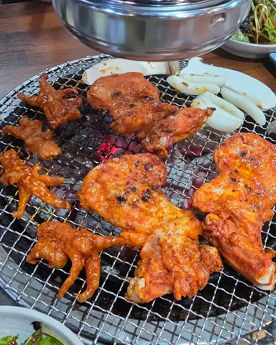 숯불 위에서 구워지고 있는 닭갈비와 곁들임 메뉴들