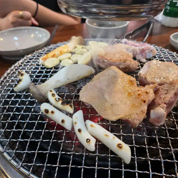 숯불 위에서 잘 익어가고 있는 닭갈비와 곁들임 메뉴들