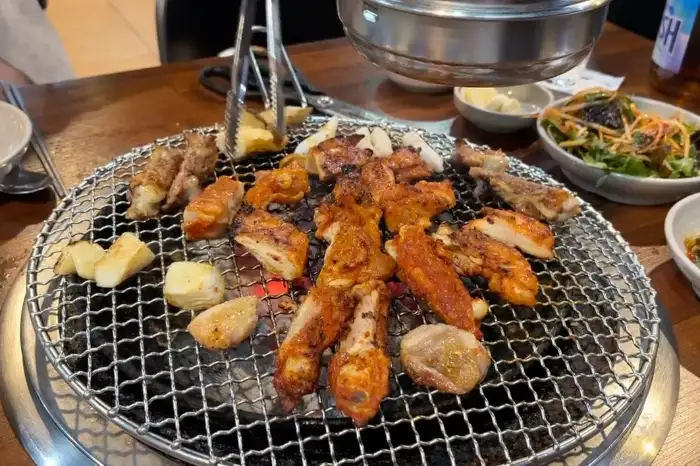 숯불 위에서 다양한 닭갈비 부위와 곁들임 메뉴가 익어가고 있습니다.