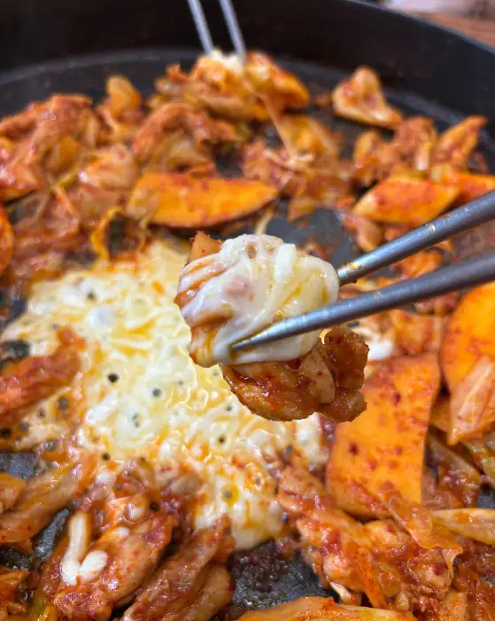 젓가락으로 집은 닭갈비 조각에 치즈가 쭉 늘어나는 모습