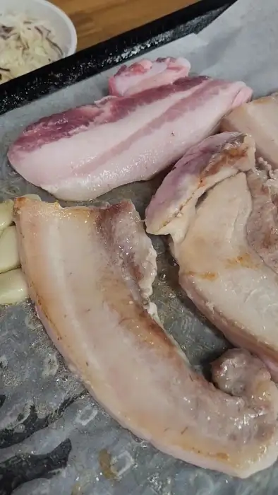 신선한 삼겹살이 불판 위에 놓여 있는 모습. 두툼한 고기와 지방층의 대비가 선명하다.
