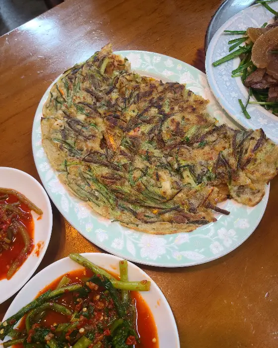 신선한 채소들이 여러 접시에 담겨 테이블 위에 놓여 있다. 다양한 종류의 쌈 채소가 준비되어 있다.