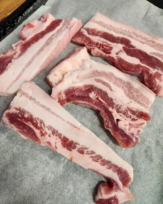 생 삼겹살 조각들이 불판 위에 놓여 있다. 지방과 살코기의 비율이 이상적이다.