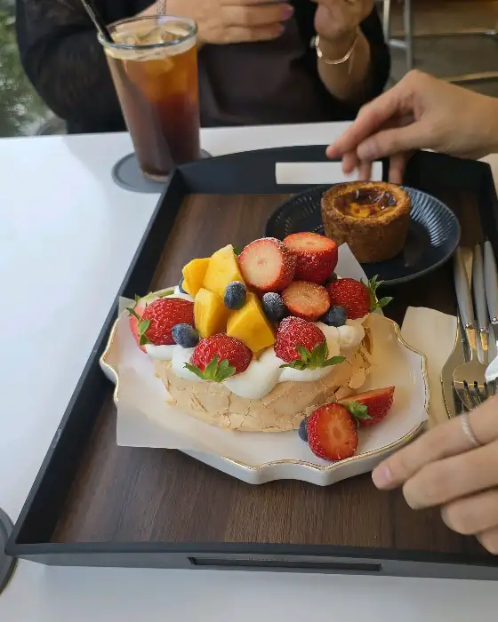 테이블 위에 놓인 파블로바 케이크와 음료, 그리고 손의 모습