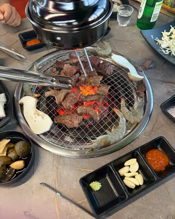 두툼한 한우 고기 조각들이 숯불 위에서 맛있게 익어가고 있는 모습