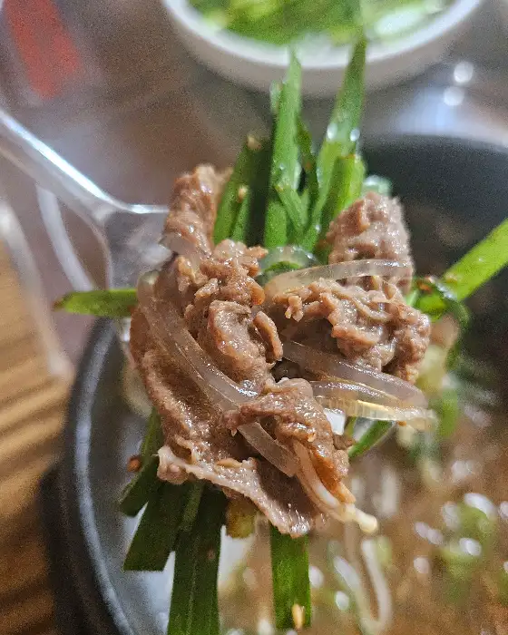 포크에 집힌 갈비살과 파채, 맑은 국물이 보인다.