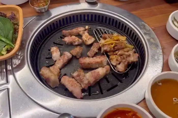 불판 위에서 삼겹살과 마늘, 쌈채소가 구워지고 있는 모습