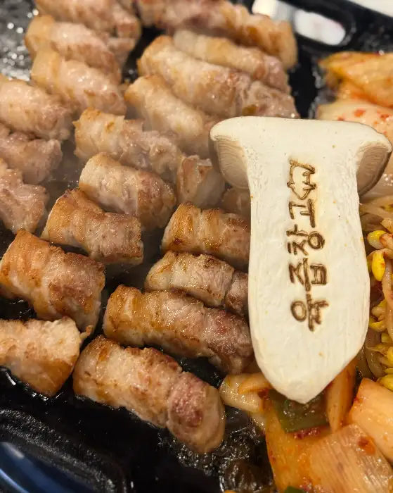 노릇하게 구워진 삼겹살과 버섯, 김치, 콩나물이 함께 담긴 철판