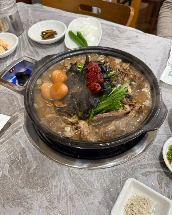 김천 능삼이네 능이백숙이 끓고 있는 솥. 붉은 양념,  яйца, 녹색 채소가 얹혀져 있어 시각적인 풍성함을 더한다.