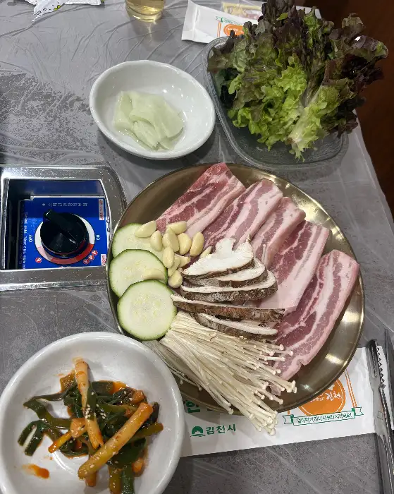 김천 능삼이네 식당 내부 테이블 세팅 사진. 깔끔한 테이블보 위로 정갈한 기본 찬과 수저 세트가 준비되어 있다.
