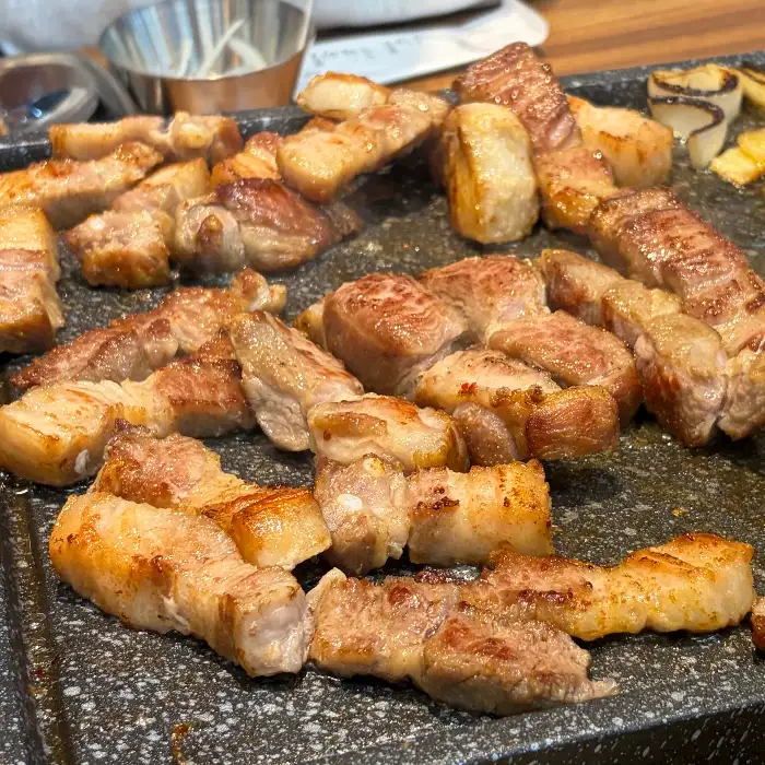 다양한 부위의 삼겹살과 목살이 불판 위에 구워지고 있는 모습