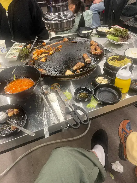 솥뚜껑 위에서 익어가는 삼겹살과 곁들임 메뉴들
