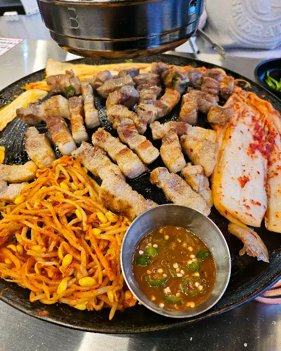 솥뚜껑 위에 올라간 삼겹살과 곁들임 채소