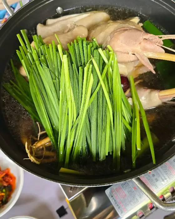 김이 모락모락 나는 능이백숙 냄비에 신선한 능이버섯과 채소가 담겨 있음