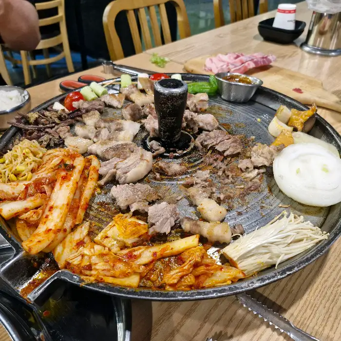 다양한 흑돼지 부위와 곁들임 재료들이 솥뚜껑 불판 위에서 구워지고 있는 모습