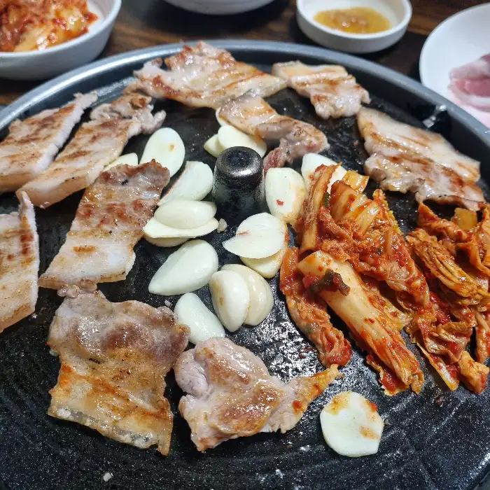 잘 구워진 삼겹살 한 점과 곁들여 먹는 마늘, 김치