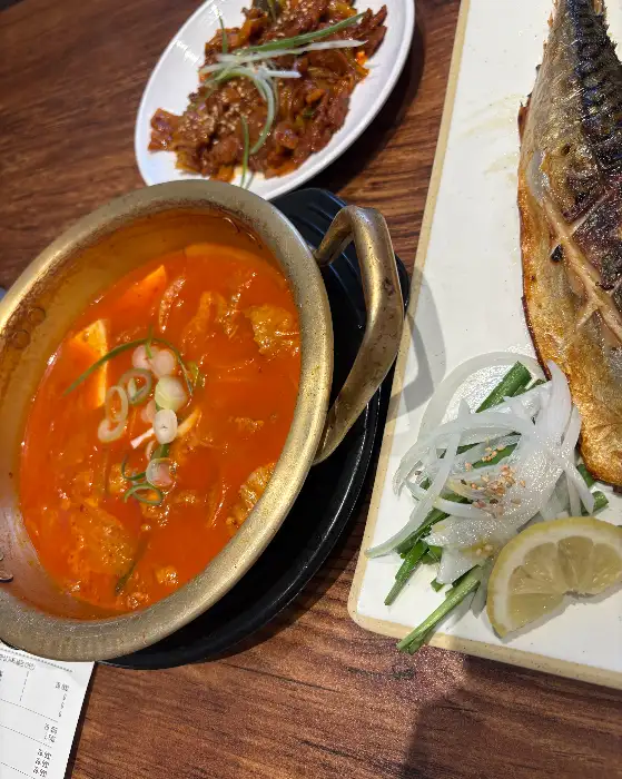 노릇하게 구워진 생선구이와 붉은 양념의 제육볶음, 뚝배기 찌개가 담긴 테이블 모습
