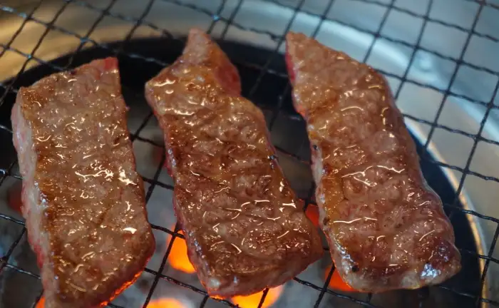 세 조각의 소고기가 석쇠 위에서 굽히고 있으며, 아래에는 연탄불이 보인다.