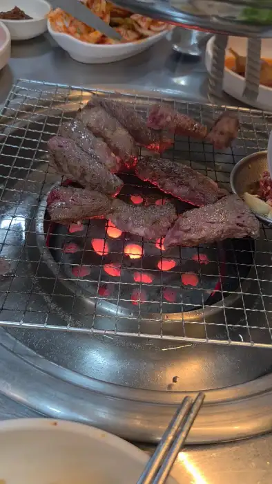 석쇠 위에서 익고 있는 여러 조각의 소고기. 아래에는 숯불이 보인다.