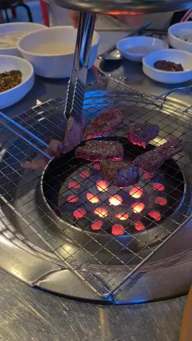 석쇠 위에 소고기를 굽고 있는 모습. 집게로 고기를 집어 불판 위에 올리고 있다.
